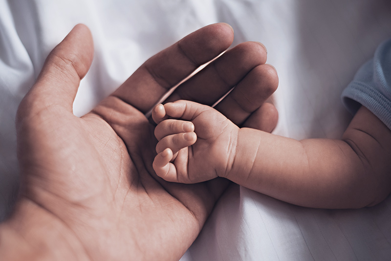 Una mano adulta sosteniendo la mano de un bebé